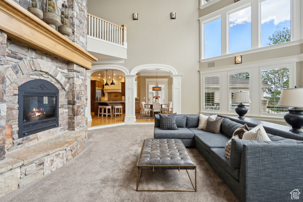 Carpeted living room featuring a towering ceiling, ornate columns, a fireplace, and arched walkways