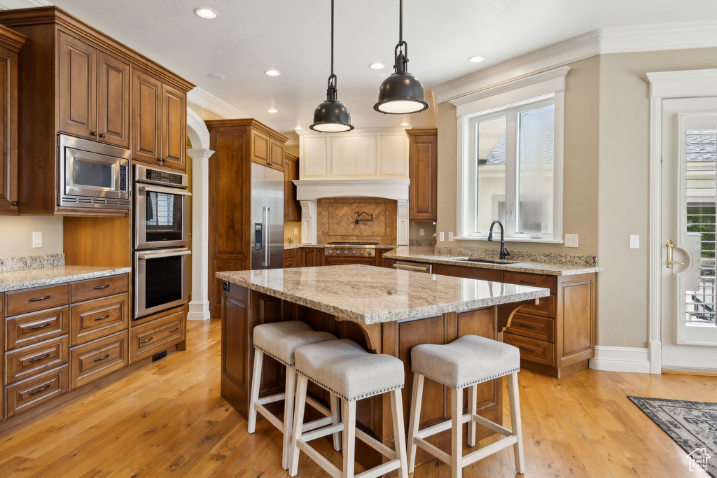 Kitchen with built in appliances, a sink, light wood finished floors, recessed lighting, and a breakfast bar area
