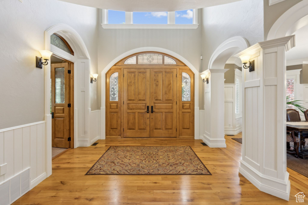 Foyer with ornate columns, a decorative wall, arched walkways, wainscoting, and a high ceiling