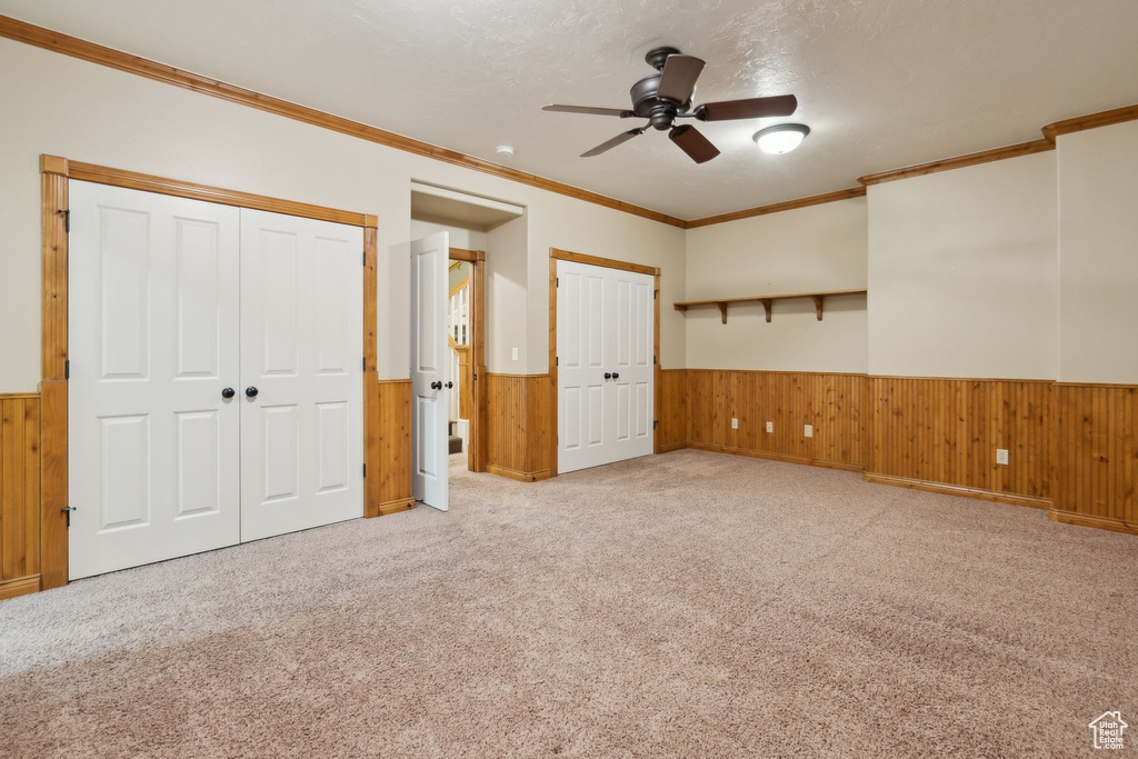Unfurnished bedroom with wainscoting, multiple closets, wood walls, carpet flooring, and ornamental molding