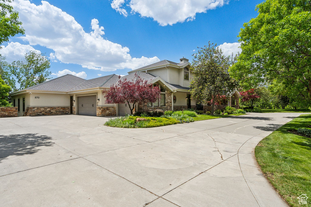 View of front of property with stucco siding, stone siding, driveway, an attached garage, and a chimney
