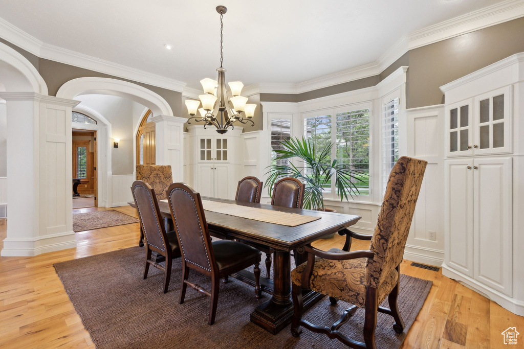 Dining room featuring decorative columns, arched walkways, a decorative wall, light wood-style flooring, and a chandelier