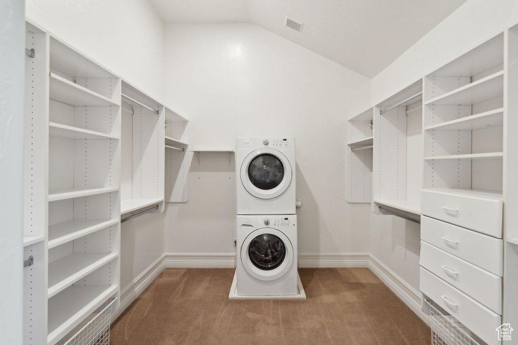 Spacious closet featuring stacked washer / drying machine, carpet, and vaulted ceiling
