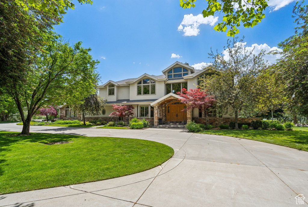 View of front of house with stucco siding, curved driveway, stone siding, and a front yard