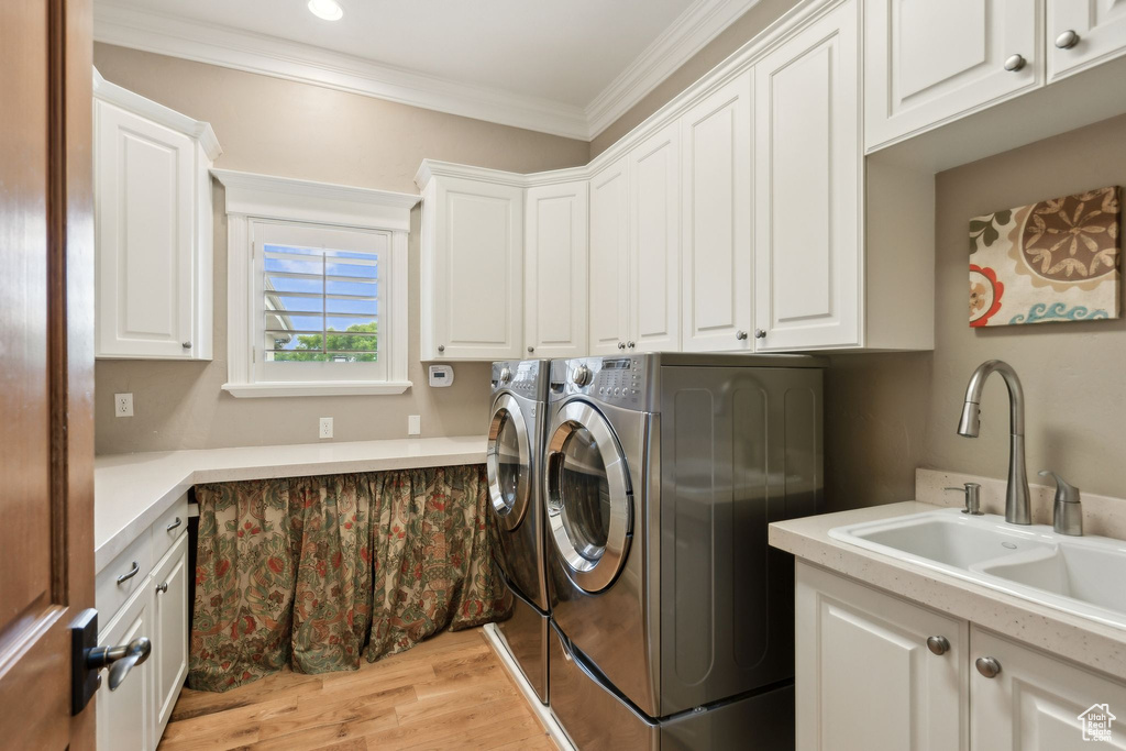 Laundry room featuring cabinet space, washer and dryer, crown molding, and light wood-style flooring