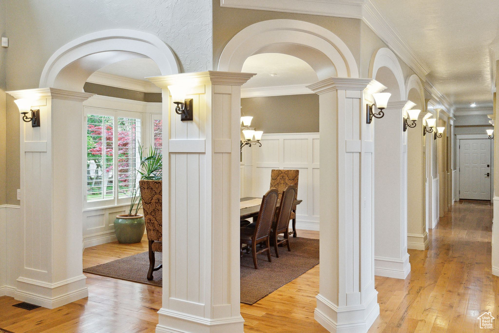 Hall with a decorative wall, light wood-style floors, ornamental molding, arched walkways, and a wainscoted wall