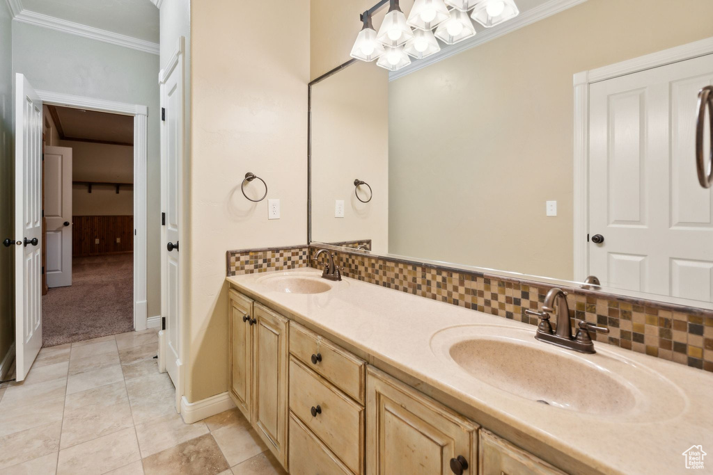 Full bath with crown molding, double vanity, tasteful backsplash, tile patterned floors, and baseboards