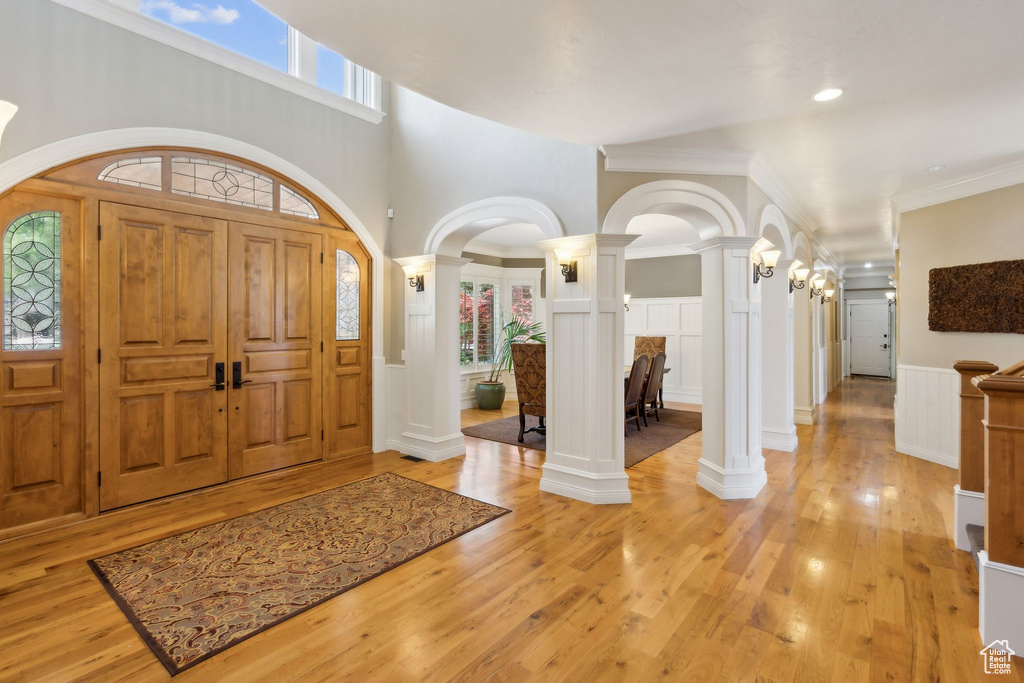 Foyer with decorative columns, light wood finished floors, wainscoting, arched walkways, and a decorative wall