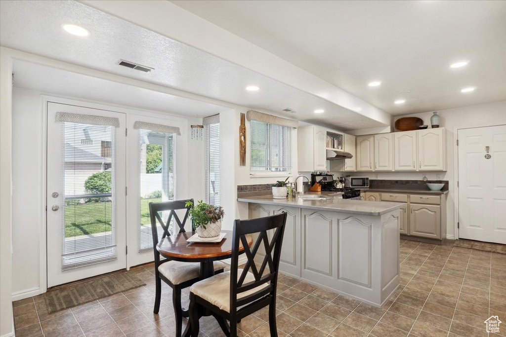 Kitchen featuring a peninsula, stainless steel microwave, under cabinet range hood, a sink, and recessed lighting
