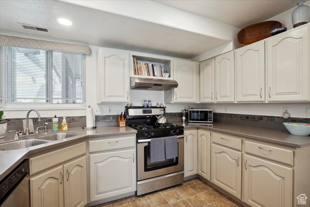 Kitchen featuring stainless steel appliances, under cabinet range hood, a sink, recessed lighting, and dark countertops