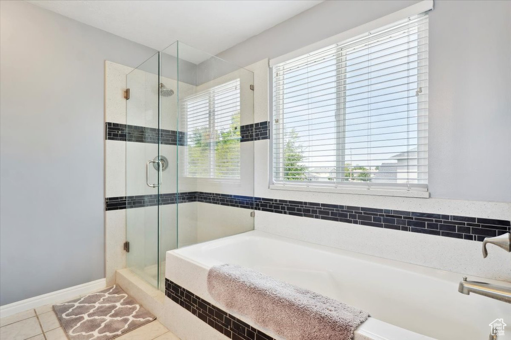 Full bathroom featuring a bath, a stall shower, tile patterned flooring, and baseboards