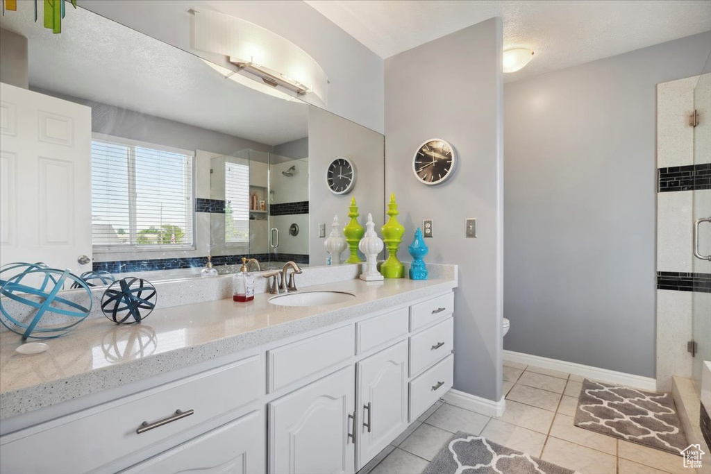 Bathroom featuring a tile shower, vanity, toilet, tile patterned flooring, and baseboards