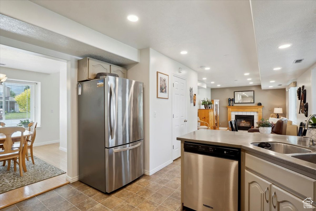 Kitchen with appliances with stainless steel finishes, a tiled fireplace, recessed lighting, a sink, and baseboards