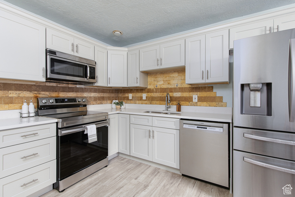 Kitchen featuring appliances with stainless steel finishes, a sink, light countertops, tasteful backsplash, and a textured ceiling