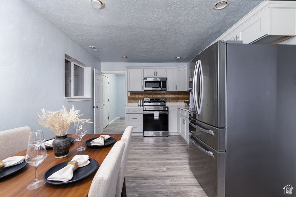 Kitchen with appliances with stainless steel finishes, a textured ceiling, wood finished floors, decorative backsplash, and white cabinets