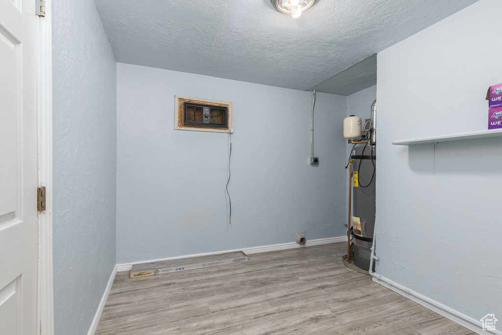 Laundry room featuring wood finished floors, a textured ceiling, water heater, baseboards, and a wall mounted AC
