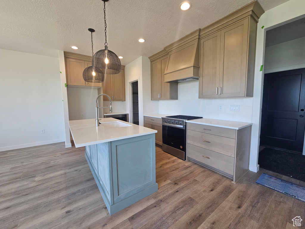 Kitchen with stainless steel range with gas cooktop, custom range hood, light wood-type flooring, a sink, and recessed lighting