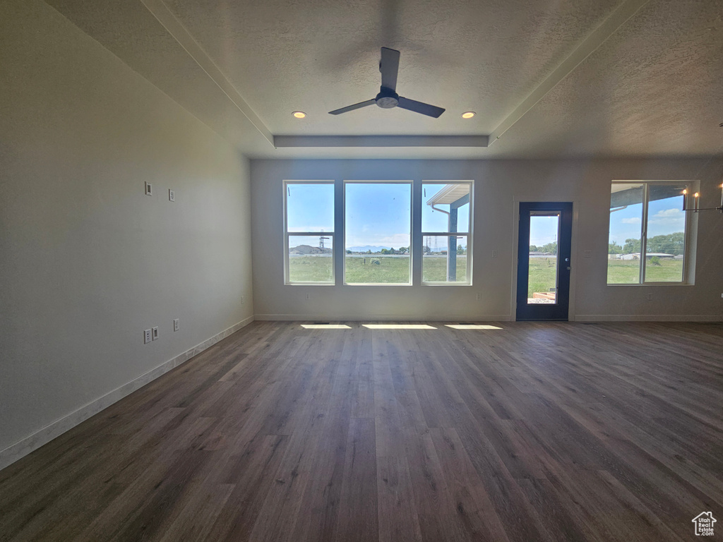 Unfurnished living room with dark wood-style flooring, healthy amount of natural light, baseboards, a textured ceiling, and a tray ceiling