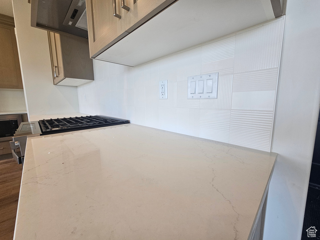 Kitchen view of light stone countertops, stainless steel microwave, stovetop, exhaust hood, and tasteful backsplash