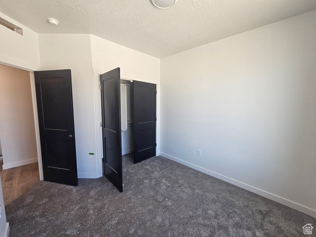 Unfurnished bedroom featuring dark colored carpet, baseboards, and a closet