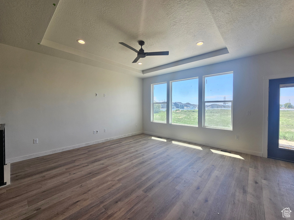 Empty room with a raised ceiling, a textured ceiling, wood finished floors, a ceiling fan, and baseboards