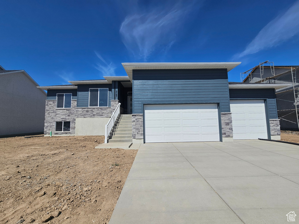 View of front of home featuring stone siding, a garage, and driveway