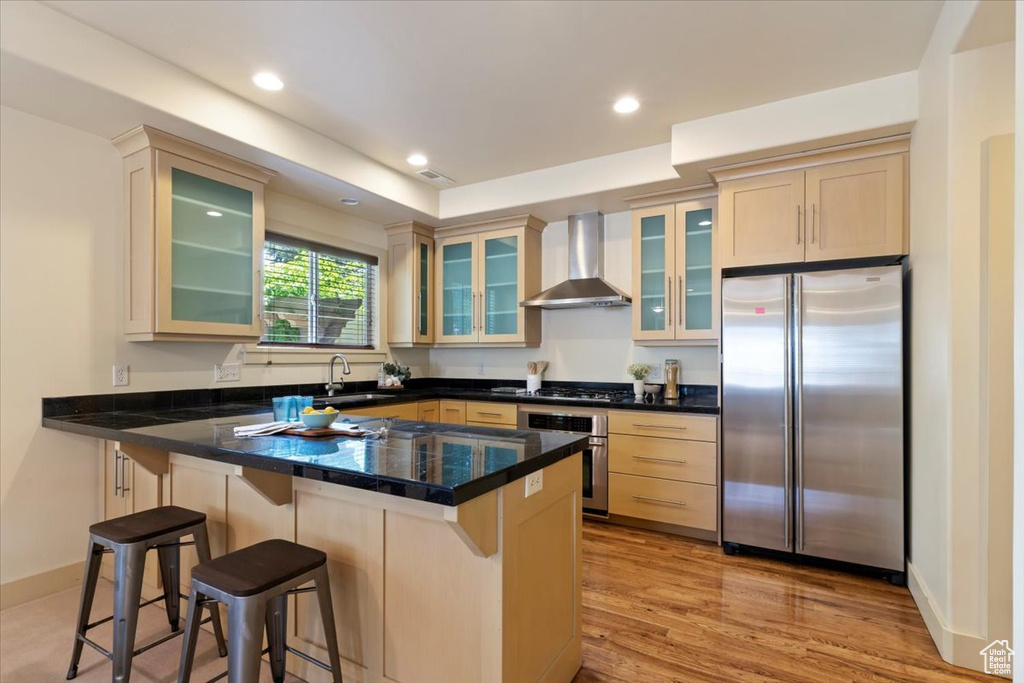 Kitchen featuring appliances with stainless steel finishes, wall chimney exhaust hood, a peninsula, a breakfast bar, and a sink