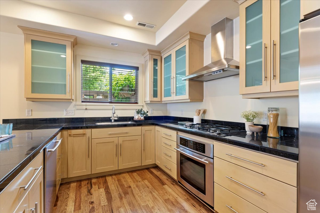 Kitchen with stainless steel appliances, wall chimney exhaust hood, a sink, light wood-type flooring, and recessed lighting