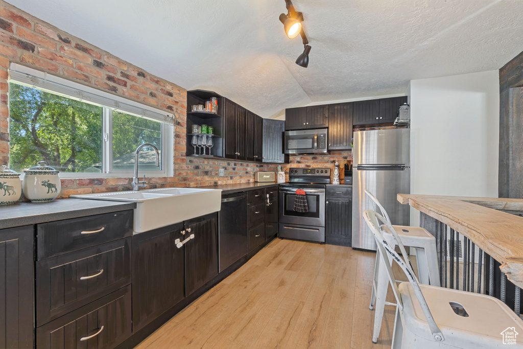 Kitchen with appliances with stainless steel finishes, light wood-style floors, a sink, brick wall, and open shelves
