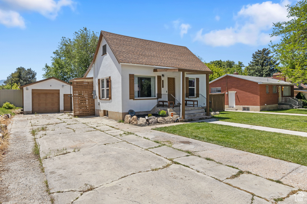 View of front of house featuring an outbuilding, a porch, a shingled roof, a front lawn, and stucco siding