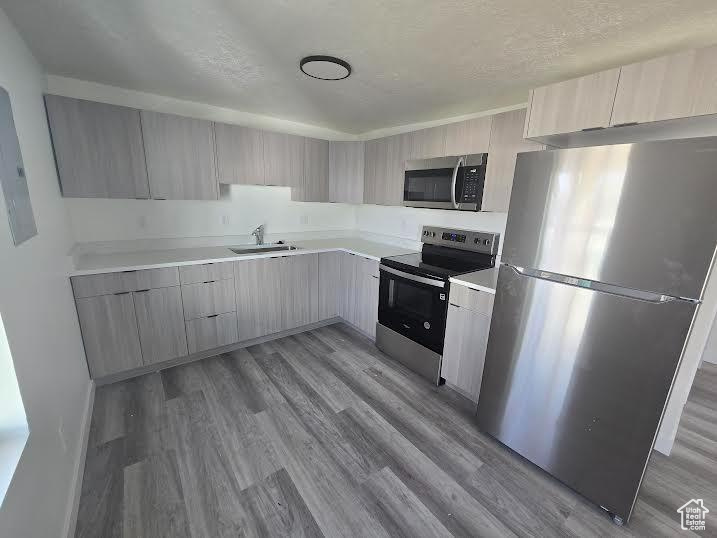 Kitchen with appliances with stainless steel finishes, modern cabinets, light wood-style flooring, light countertops, and a sink