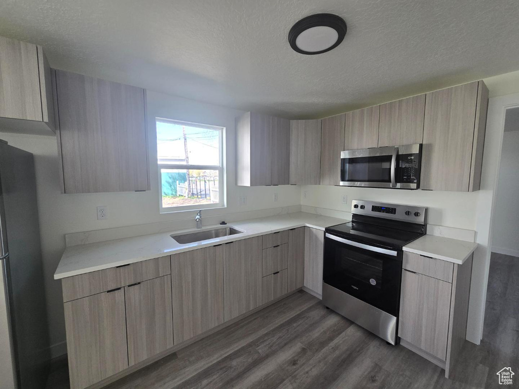 Kitchen with appliances with stainless steel finishes, modern cabinets, a sink, light brown cabinetry, and a textured ceiling