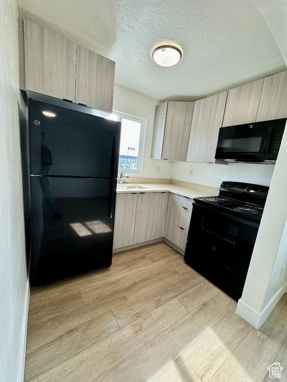 Kitchen featuring black appliances, light brown cabinetry, modern cabinets, light countertops, and light wood-type flooring