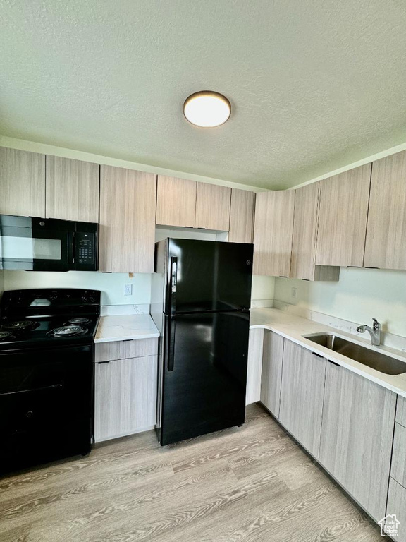 Kitchen with black appliances, light brown cabinets, a sink, a textured ceiling, and light countertops