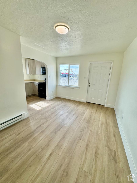 Unfurnished living room featuring arched walkways, light wood-style flooring, a textured ceiling, baseboards, and baseboard heating