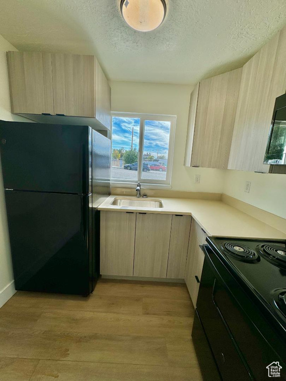 Kitchen featuring black appliances, light brown cabinets, modern cabinets, a sink, and a textured ceiling