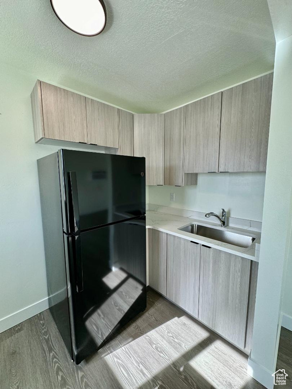 Kitchen featuring freestanding refrigerator, light brown cabinets, a sink, light countertops, and a textured ceiling