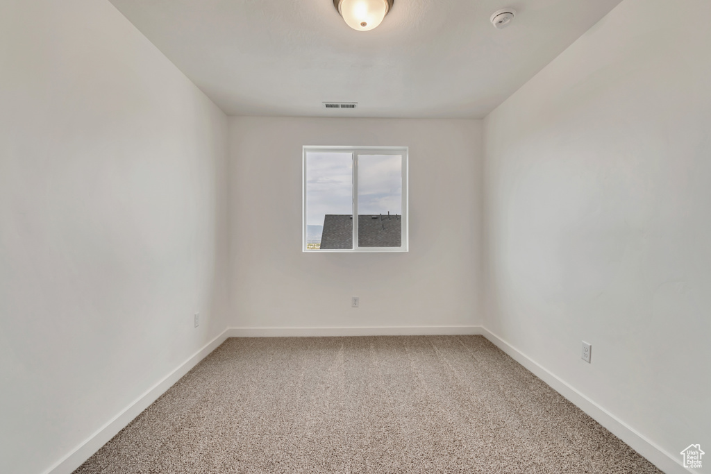 Carpeted empty room with a smoke detector and baseboards