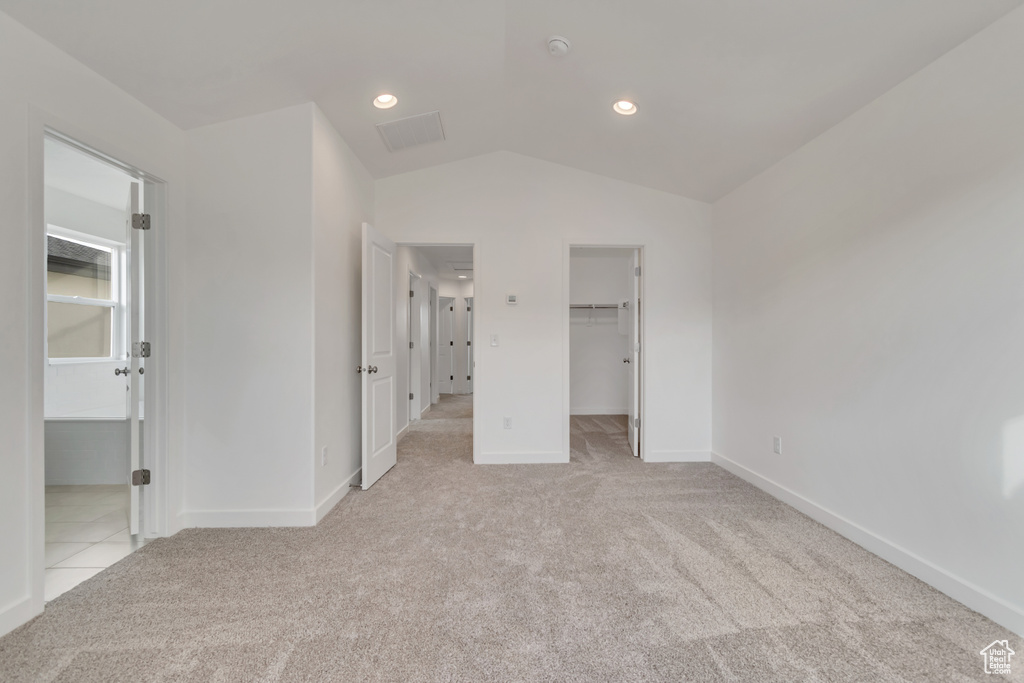 Unfurnished bedroom with light colored carpet, a spacious closet, lofted ceiling, and a closet