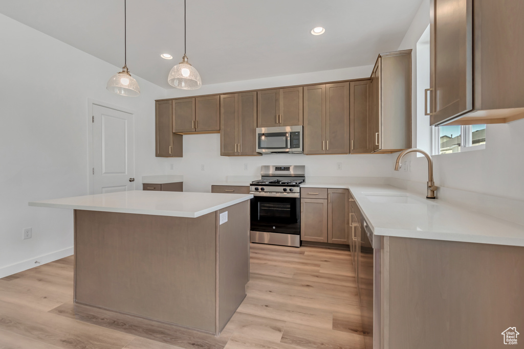 Kitchen with appliances with stainless steel finishes, light wood-style floors, a kitchen island, recessed lighting, and decorative light fixtures