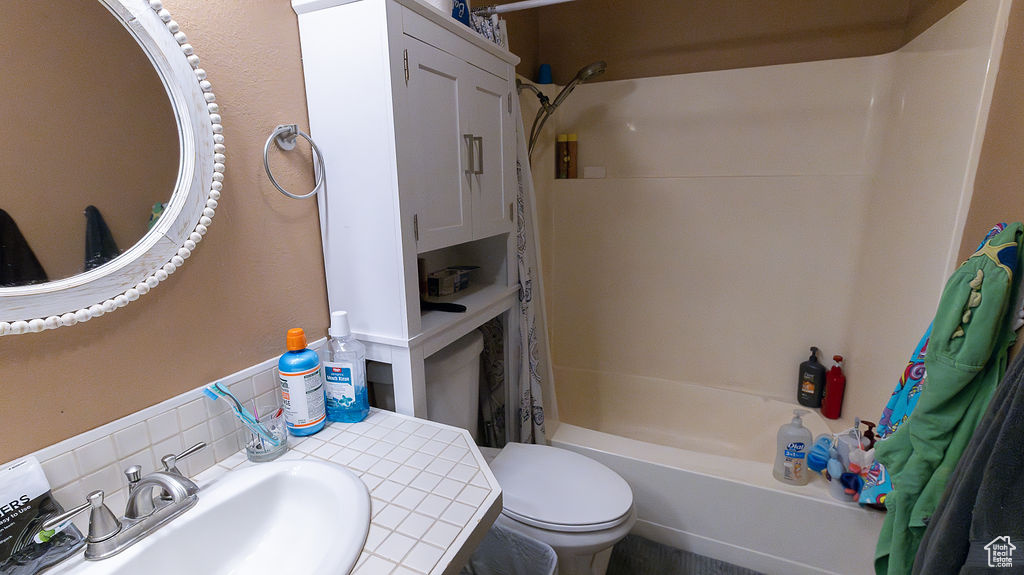 Bathroom featuring backsplash, shower / bathtub combination with curtain, and vanity