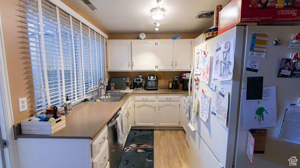 Kitchen with freestanding refrigerator, a sink, dishwasher, white cabinetry, and light wood-type flooring