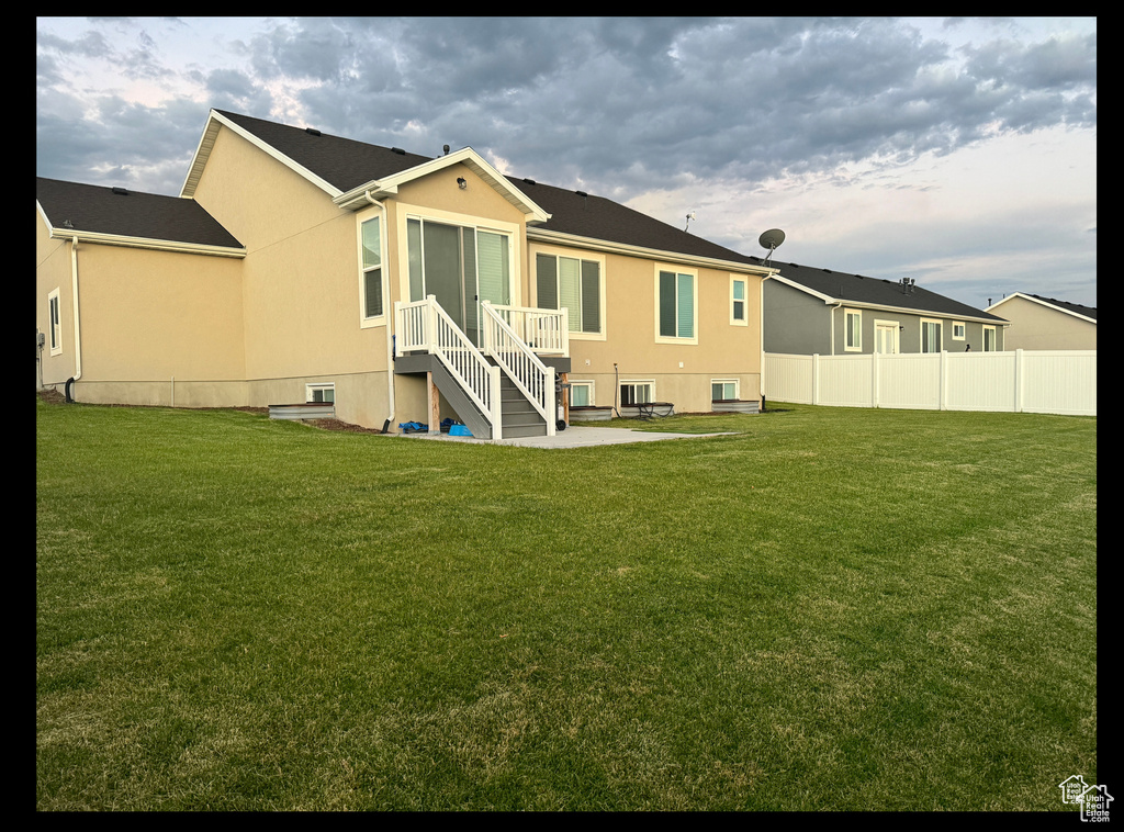 Rear view of property featuring a lawn, fence, and stucco siding