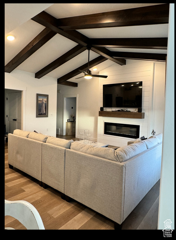 Living room featuring ceiling fan, vaulted ceiling with beams, a glass covered fireplace, and wood finished floors