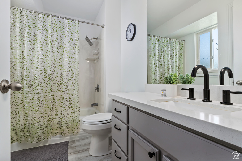 Full bath featuring vanity, toilet, shower / bath combo, and wood finished floors