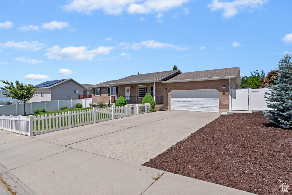 Ranch-style house featuring brick siding, an attached garage, concrete driveway, a fenced front yard, and a shingled roof