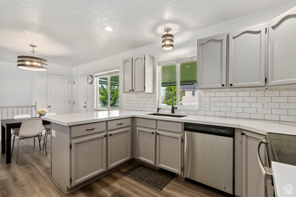 Kitchen with dishwasher, a peninsula, a sink, tasteful backsplash, and dark wood-style floors