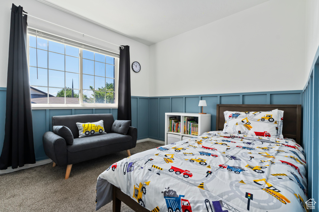 Carpeted bedroom featuring a decorative wall and a wainscoted wall