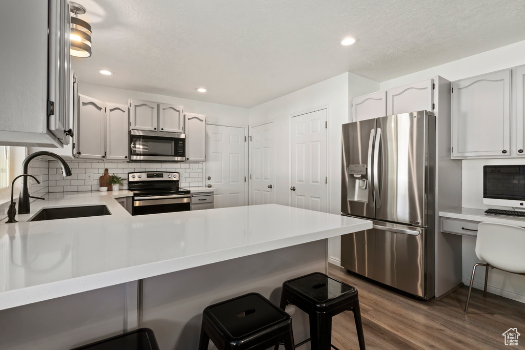 Kitchen with appliances with stainless steel finishes, a sink, dark wood finished floors, a peninsula, and backsplash