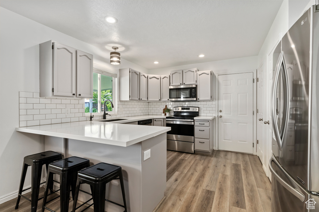 Kitchen with stainless steel appliances, a sink, a peninsula, a breakfast bar, and light wood-type flooring